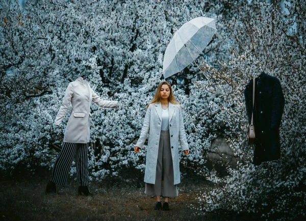 Une femme se tient dans un jardin fleuri parmi des mannequins et un parasol — Photo