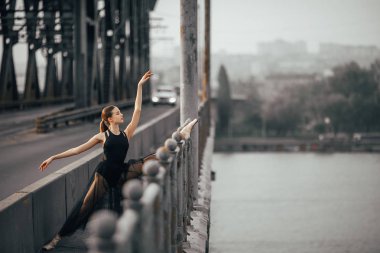 Ballerina sitting in twine pose on the bridge through the river. clipart