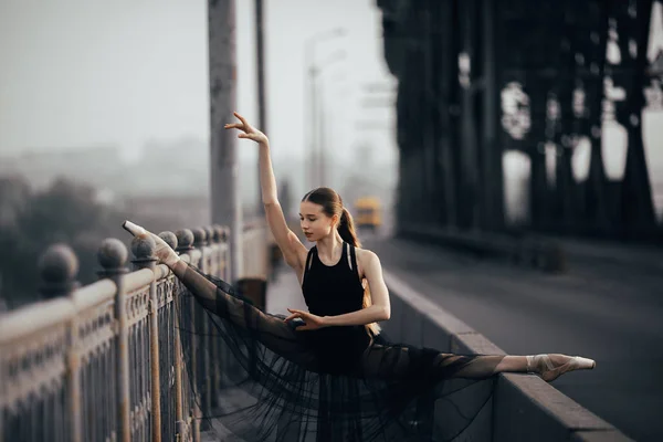 Ballerina sitting in twine pose on the bridge against the backgr