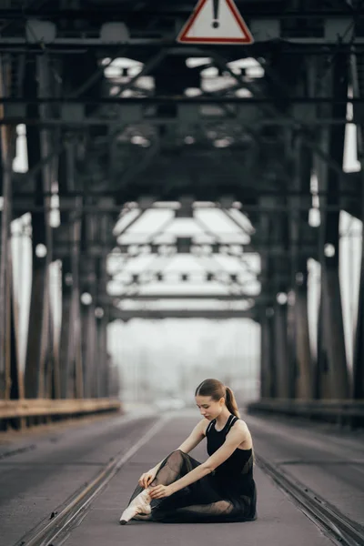 Ballerina is sitting and tying her pointe shoes between rails on