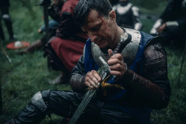 一个年轻人坐在一个中世纪骑士的形象，并清理他的剑. — 图库照片