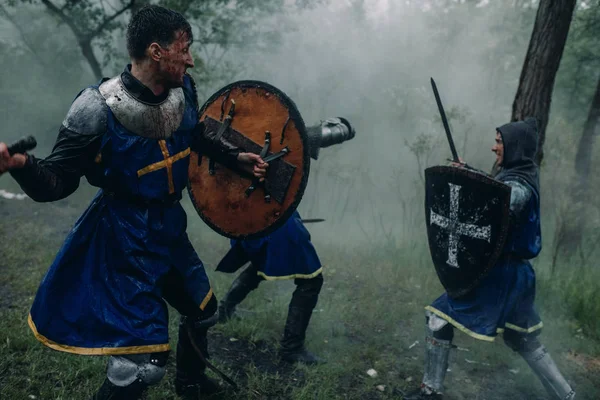 Threee men in the image of a medieval knights crusaders fight with swords. — Stock Photo, Image