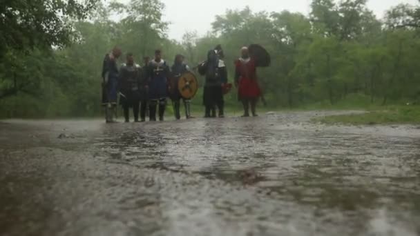 十字軍の中世の騎士の戦いの分隊は鎧に行くと雨の中で森の道路上の水たまりを通して剣を持ちます — ストック動画