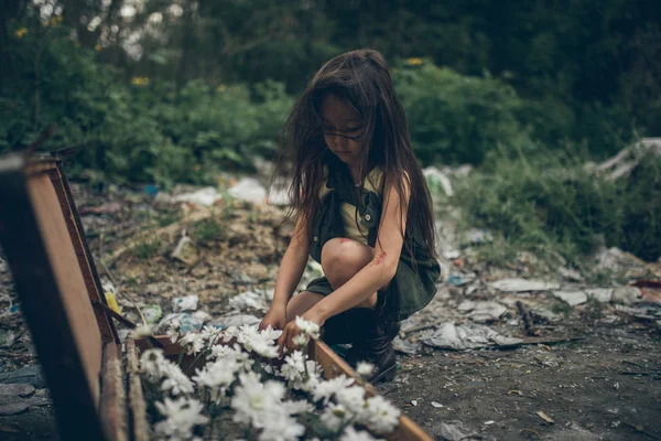 Una chica sin hogar está plantando flores en una maleta en un basurero . —  Fotos de Stock