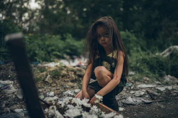 Uma menina sem-teto está plantando flores em uma mala em um depósito de lixo . — Fotografia de Stock