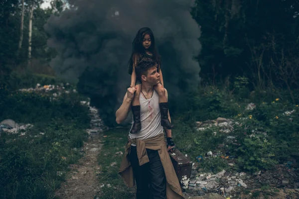 Homeless father and daughter walk through the garbage dump on background of smoke. — Stock Photo, Image