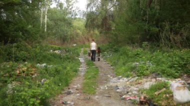 Evsiz baba ve kızı orman yolu boyunca çöplükten geçiyorlar. Çevre kirliliği, yoksulluk ve evsizlik kavramı.