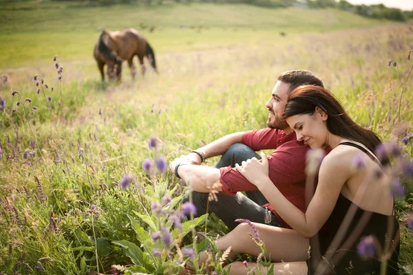 A young couple is resting in a meadow against the background of — Stock Photo, Image