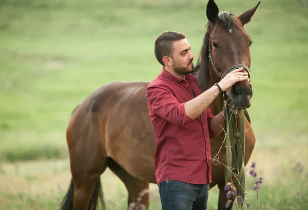 Un joven parado en un prado junto a un caballo . — Foto de Stock