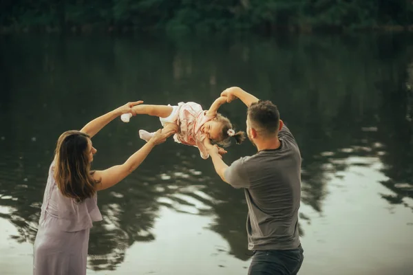 Des parents heureux jouent avec leur fille près du lac . — Photo