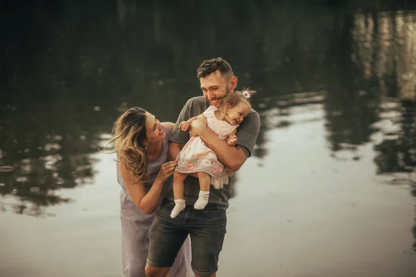 Glückliche Eltern spielen mit ihrer Tochter am See. — Stockfoto