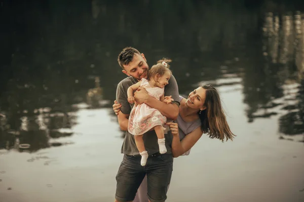 Padres felices juegan con su hija al lado del lago . — Foto de Stock