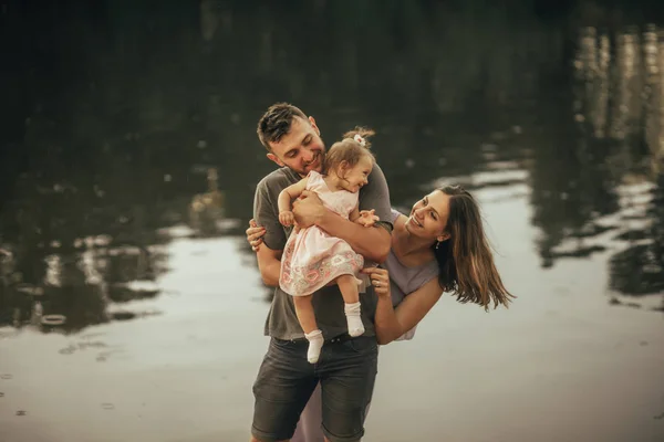 Happy parents play with their daughter next to the lake.