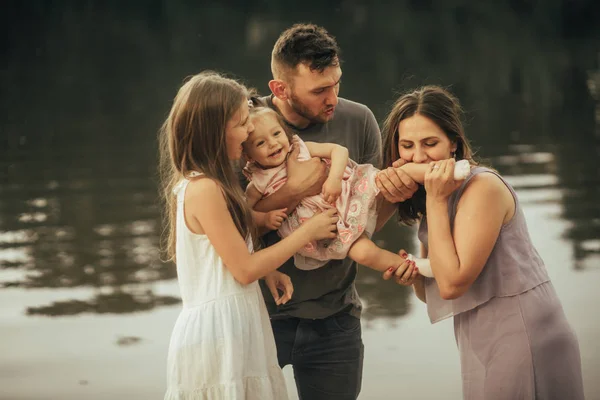 Šťastní rodiče si hrají se svou dcerou vedle jezera. — Stock fotografie