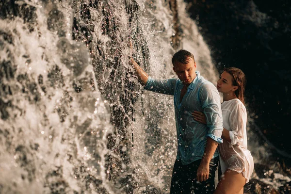 Casal abraçando sob os riachos de uma cachoeira . — Fotografia de Stock