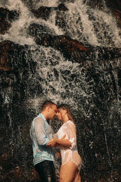 情侣拥抱在瀑布的溪流下. — 图库照片