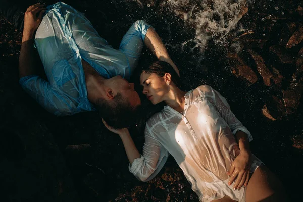 Wet couple lying and embracing on the shore in the water.