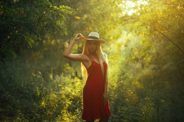 Eine junge Frau steht im von der Sonne erleuchteten Wald. — Stockfoto