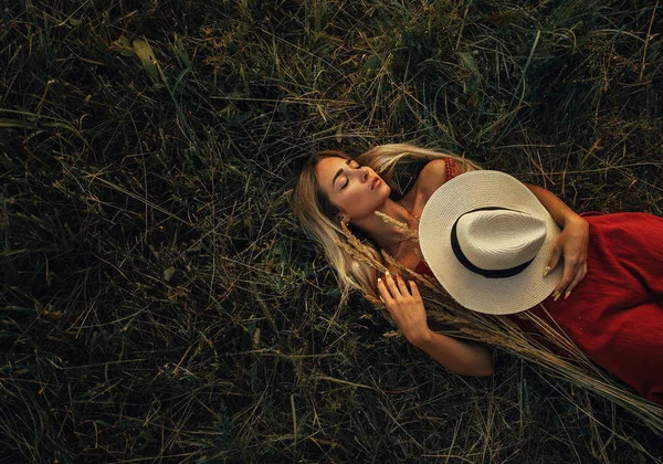 年轻的金发女子戴着帽子躺在草地上的草耳朵. — 图库照片