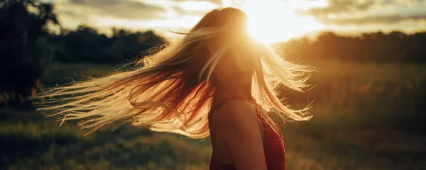 Mujer rubia joven se para en el prado con el pelo suelto iluminado por el sol . —  Fotos de Stock
