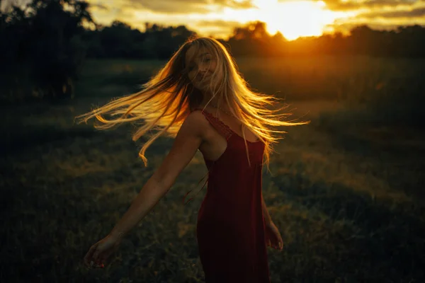 Mulher loira jovem fica no prado com cabelo solto iluminado pelo sol . — Fotografia de Stock