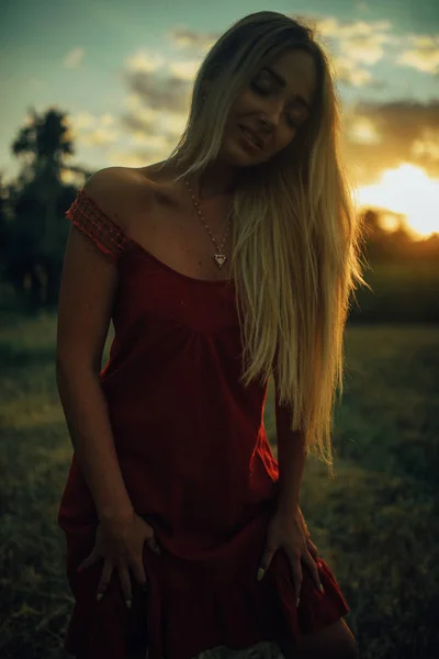 Jovem mulher fica no prado com cabelo solto ao pôr do sol . — Fotografia de Stock