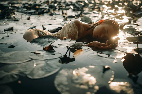 Giovane donna sdraiata nell'acqua tra le foglie e i fiori di y — Foto Stock