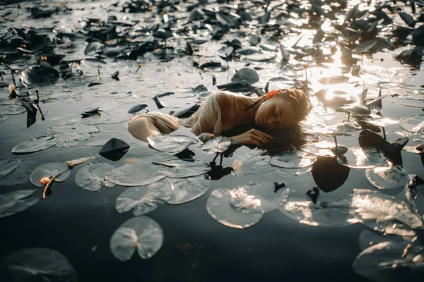 Giovane donna sdraiata nell'acqua tra le foglie e i fiori di y — Foto Stock