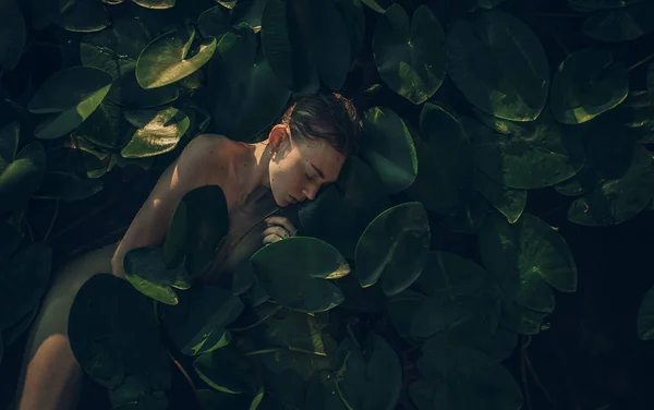 Giovane donna sdraiata nell'acqua tra le foglie di ninfee . — Foto Stock