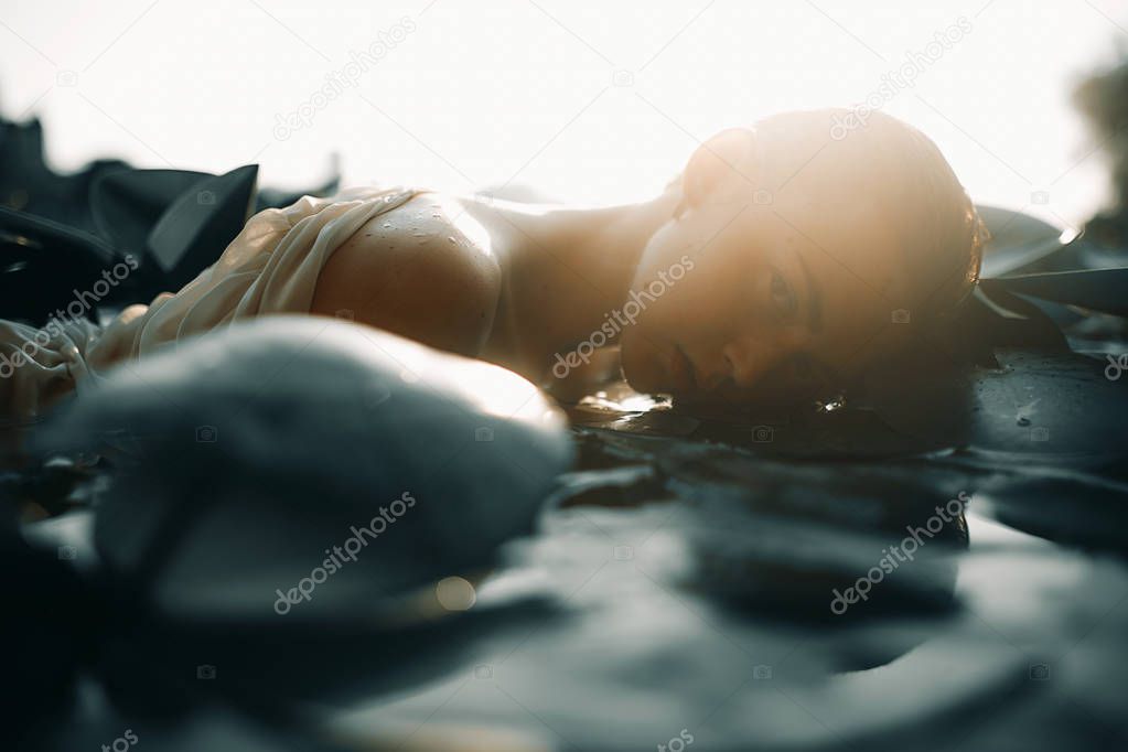 Young woman lying in the water among the leaves of water lily.