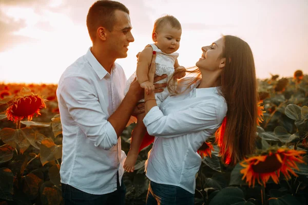 Glückliche Familie mit Baby hat Spaß und spielt im Sonnenblumenfeld. — Stockfoto