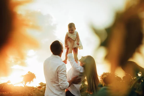 Glückliche Familie mit Baby hat Spaß und spielt im Sonnenblumenfeld. — Stockfoto