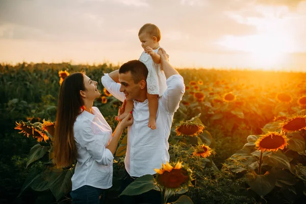 Glückliche Familie mit Baby hat Spaß und spielt im Sonnenblumenfeld. — Stockfoto