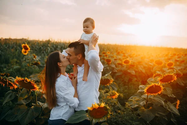 Glückliche junge Eltern mit Babyküssen im Sonnenblumenfeld. — Stockfoto