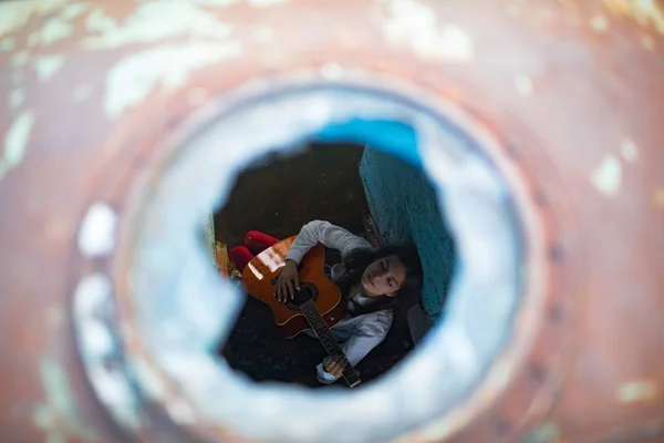 Una giovane donna siede e suona la chitarra all'interno della vecchia nave abbandonata . — Foto Stock