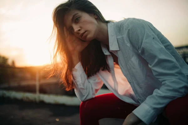 Uma jovem mulher triste senta-se com o cabelo solto ao pôr do sol . — Fotografia de Stock