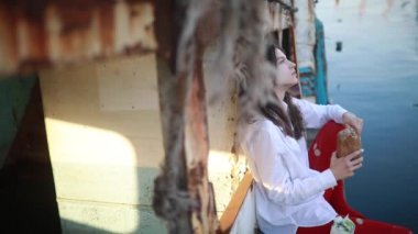 Genç bir kadın oturur ve beyaz gömlek ve kırmızı delikli tayt eski bir terk edilmiş gemide ekmek somun yiyor.
