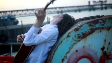 Genç bir kadın yalan söyler, gitar çalar ve beyaz gömlek ve kırmızı taytla terk edilmiş eski bir gemide şarkı söyler.. 
