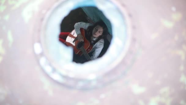 一位年轻女子坐在旧废弃的船上弹吉他 通过船口查看 — 图库视频影像