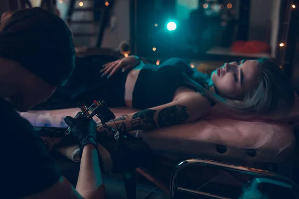 Tattoo artist creates a tattoo on a girl's arm in tattoo parlour — Stock Photo, Image