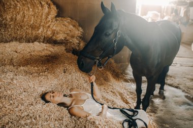 Kadın ayakta duran bir atın yanında odun talalarının üzerinde yatıyor..