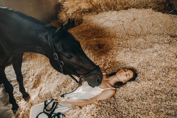 Mulher está em uma pilha de aparas de madeira ao lado de um cavalo de pé . — Fotografia de Stock