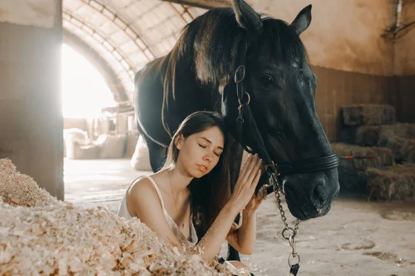 Mulher senta-se em uma pilha de aparas de madeira ao lado de um cavalo de pé . — Fotografia de Stock