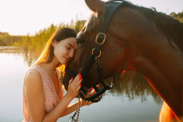 女性は川の背景に対して馬の隣に立っている. — ストック写真