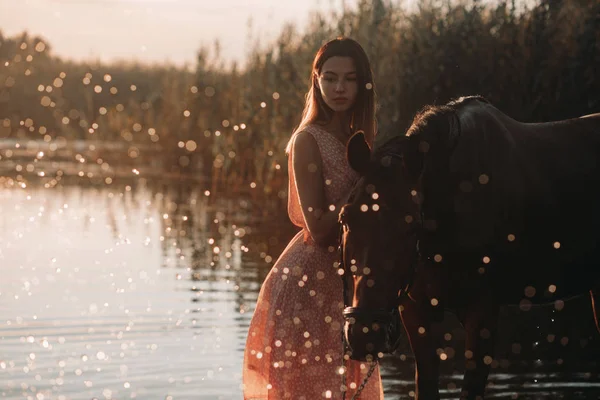 Mulher fica ao lado do cavalo contra fundo do rio a — Fotografia de Stock