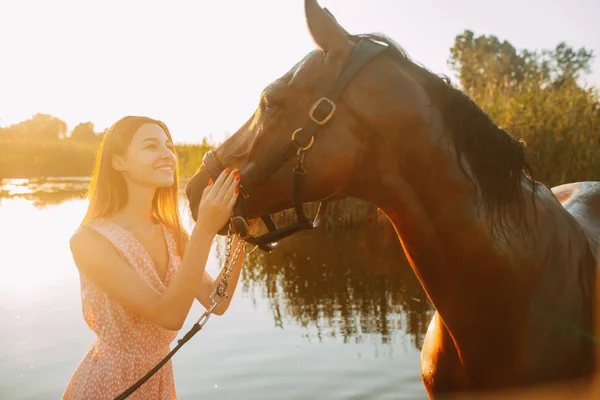 女性は川の背景に対して馬の隣に立っている. — ストック写真