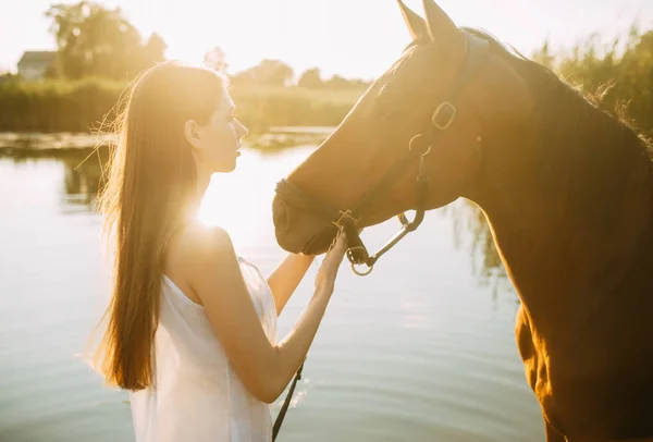 女性は日没時に川の馬の隣に立つ. — ストック写真