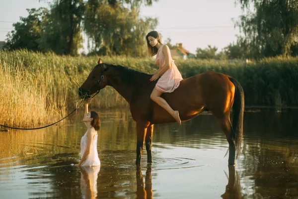 Mulher se senta montado um cavalo e outra mulher banha-se no rio . — Fotografia de Stock