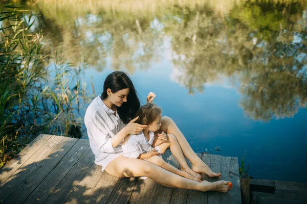 Mor och dotter sitter på en träbro över en flod. — Stockfoto