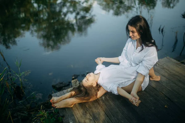 Matka a dcera se baví na dřevěném mostě blízko řeky. — Stock fotografie